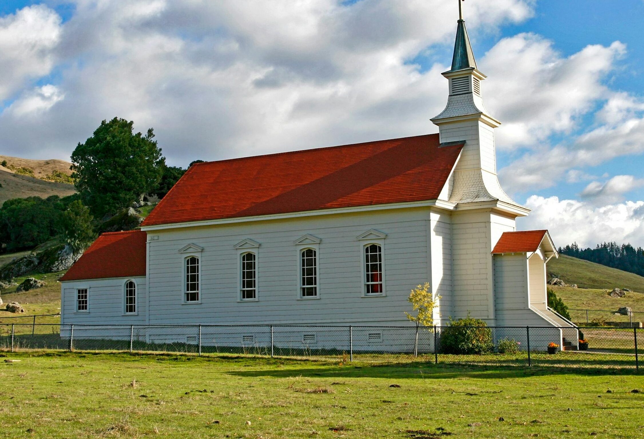 Charming rural church with red roof and steeple against a picturesque countryside backdrop.